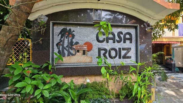 Μια επιγραφή με την ονομασία «CASA ROIZ» και ένα τοιχογραφημένο σχέδιο που απεικονίζει ένα άτομο και ένα φοινικόδεντρο.