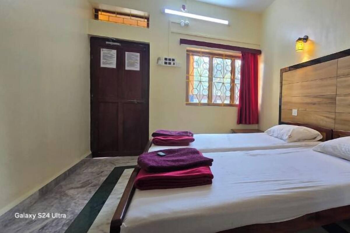 Habitación de hotel con dos camas, cabecera de madera, ventana con cortina roja y puerta con un cartel.