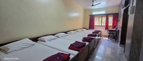 A hotel room with multiple Galaxy S24 Ultra beds, a dining table, and a window with red curtains.