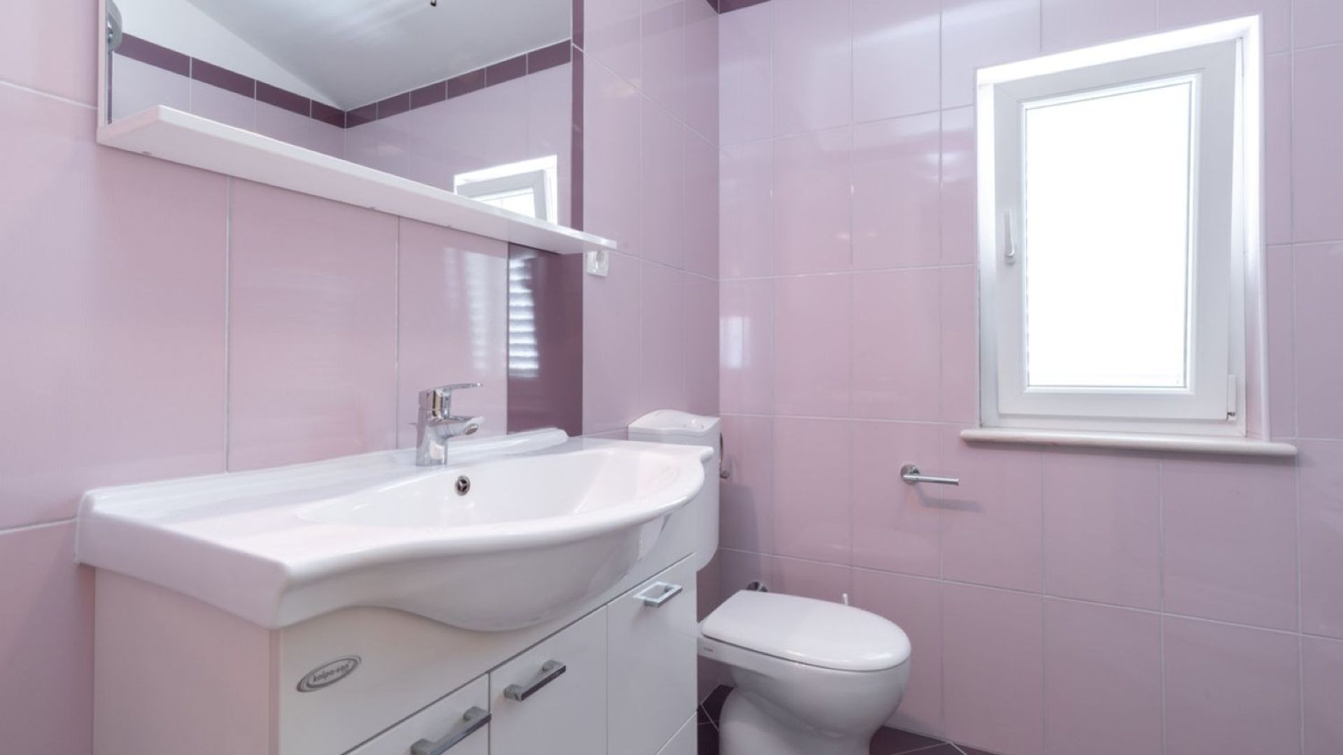 A bathroom with a white sink, mirror, and toilet.