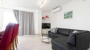 Ein modernes Wohnzimmer mit einer schwarzen Couch, einem Fernseher auf einem Holzboden, einem roten Sessel und einem Glastisch.