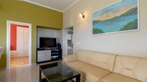 Ein Wohnzimmer mit einem beigefarbenen Sofa, einem Flachbildfernseher, einem Couchtisch und einem Gemälde einer Küstenlandschaft.
