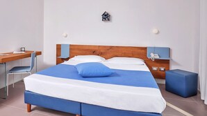 A bedroom with a wooden headboard, a bed with blue and white bedding, a desk with a chair, a small bedside table with a lamp, and a wall-mounted telephone. - A cozy space ideal for two people, designed for comfort and tranquility. The sleeping area can be arranged with a double bed or twin beds, depending on the guests' needs.Most units feature a veranda or garden furnished with a table and chairs, perfect fo (Porto San Paolo)