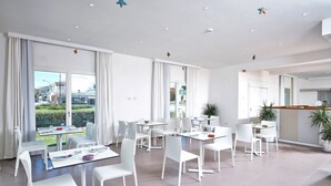 A modern hotel room with a large window, a dining area with white furniture, and a view of the cityscape. - A cozy space ideal for two people, designed for comfort and tranquility. The sleeping area can be arranged with a double bed or twin beds, depending on the guests' needs.Most units feature a veranda or garden furnished with a table and chairs, perfect fo (Porto San Paolo)