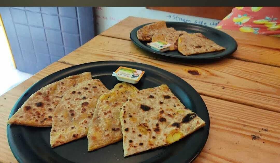 Una mesa de madera con dos porciones de paratha negro y un recipiente pequeño de mantequilla.