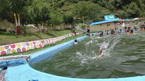 A swimming pool with a colorful border, surrounded by a fence and trees. - Nature Walk Resort Mussoorie (Mussoorie)