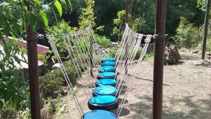 A rope bridge with blue circular platforms over a dirt path, surrounded by greenery. - Nature Walk Resort Mussoorie (Mussoorie)