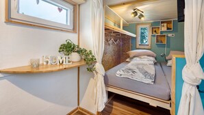 Ein gemütliches Schlafzimmer mit einem Bett, einer Kommode mit Dekoration, einem Fenster mit Vorhängen und einer Holzbalkendecke.