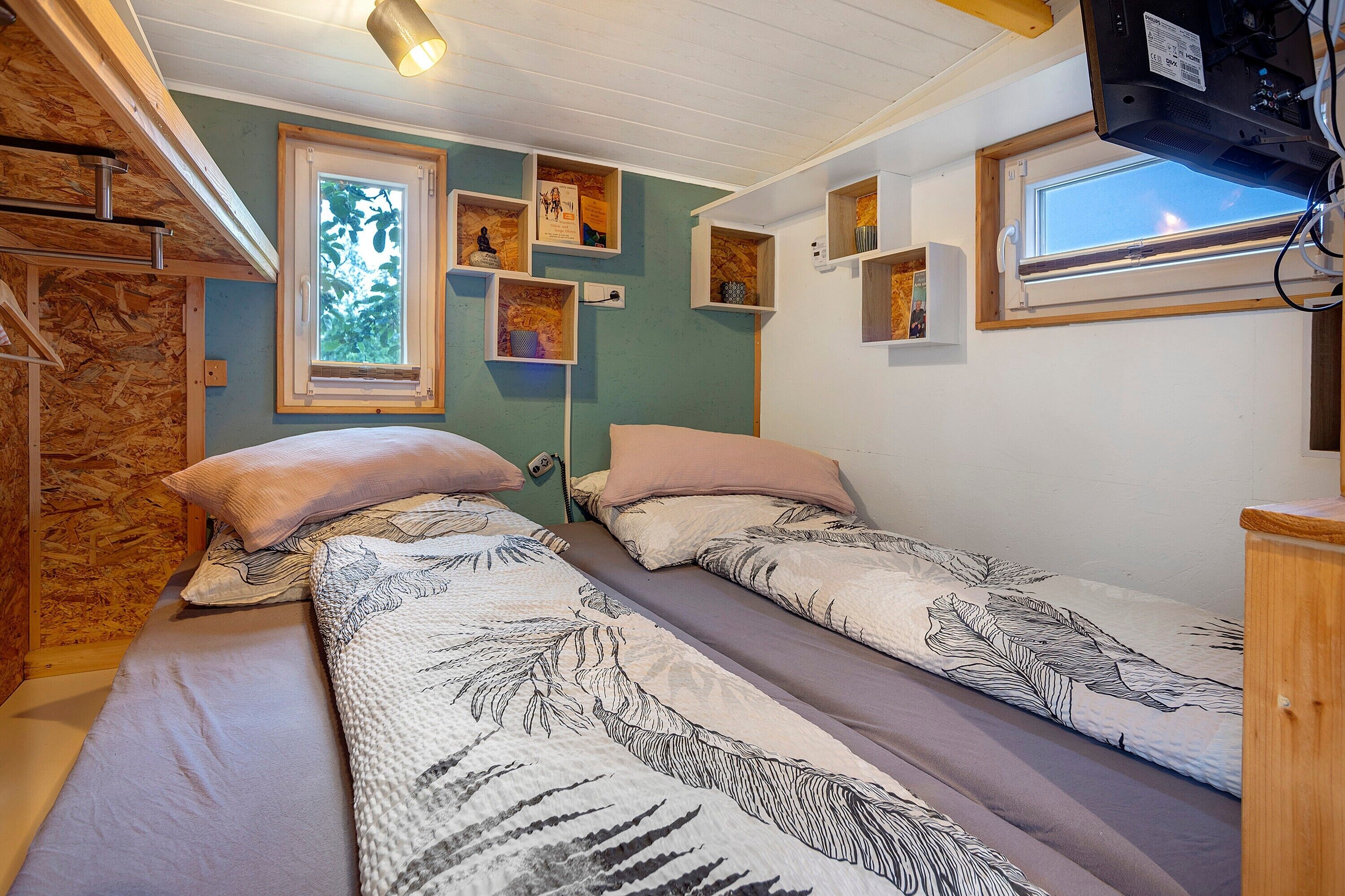 A bedroom with two beds, wooden shelves, a window, and a television.