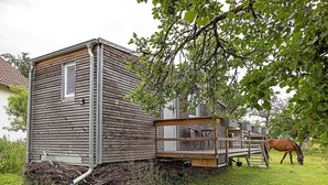 Eine Holzhütte mit Fenster und Rampe, im Hintergrund ein Pferd.