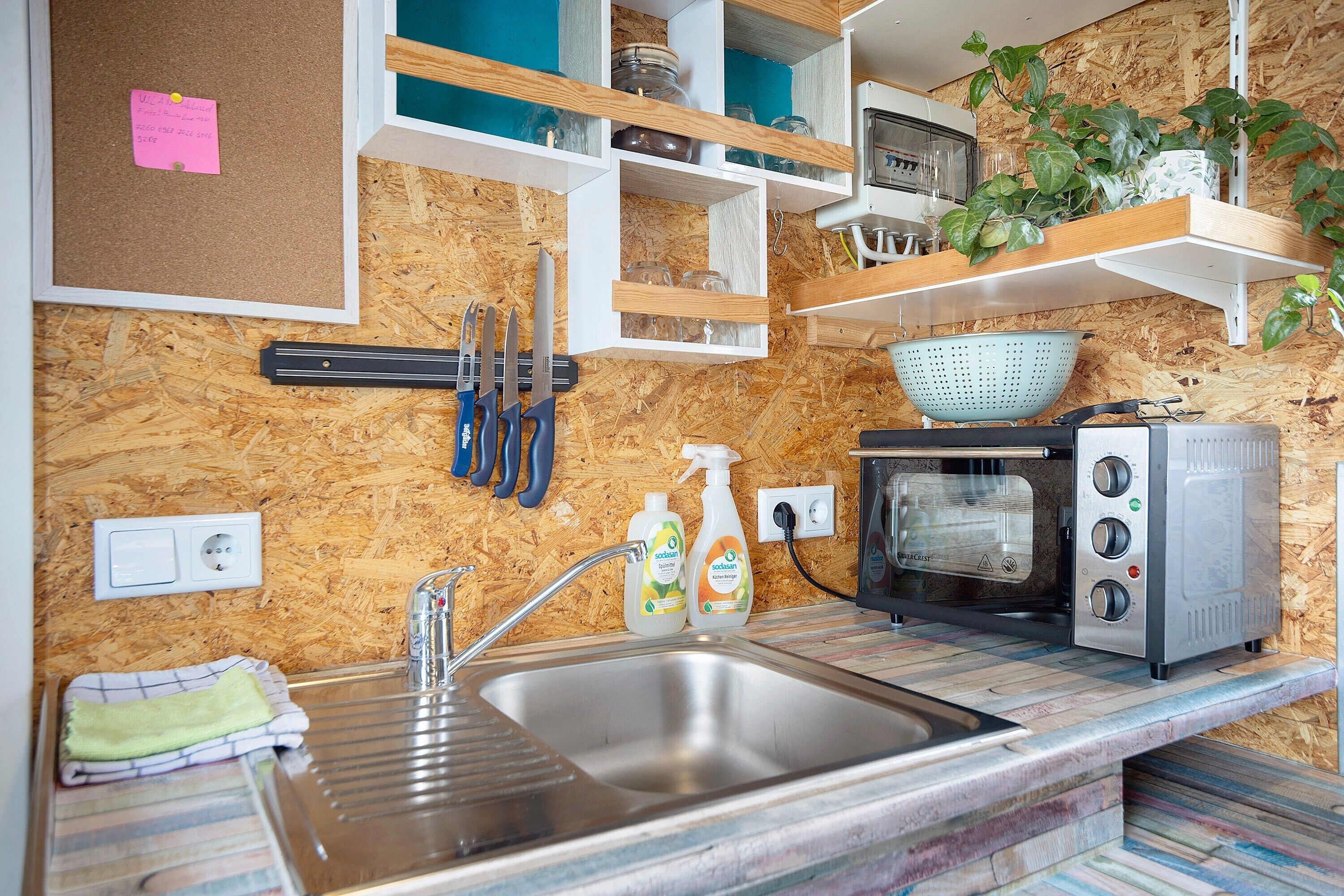 A kitchen with a built-in sink, a toaster, and shelves with jars and plants.