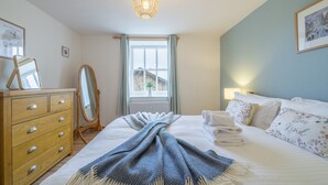 Une chambre à coucher comprenant un lit, une commode, un miroir, une fenêtre et un luminaire suspendu.
