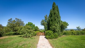 A paved pathway leading to a wooden gate, surrounded by lush greenery and tall trees. - Apartment 'Appartamento 9' with Shared Pool and Shared Garden (Lajatico)