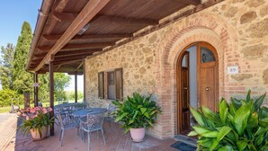 A stone building with a covered patio, outdoor seating, and potted plants. - Apartment 'Appartamento 9' with Shared Pool and Shared Garden (Lajatico)