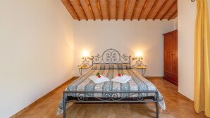 Une chambre à coucher avec un lit, des poutres apparentes en bois au plafond, une table de chevet et une armoire.