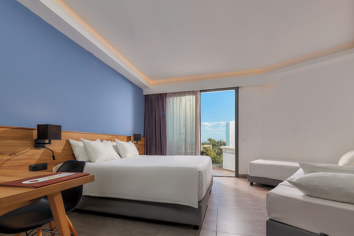 A hotel room with a bed, a desk, and a chair. There is a view of the outside through a large window.