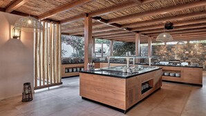 A modern kitchen area with wooden beams, a central island with a sink, and a buffet setup. - Sentido Amounda Bay (Malevizi)