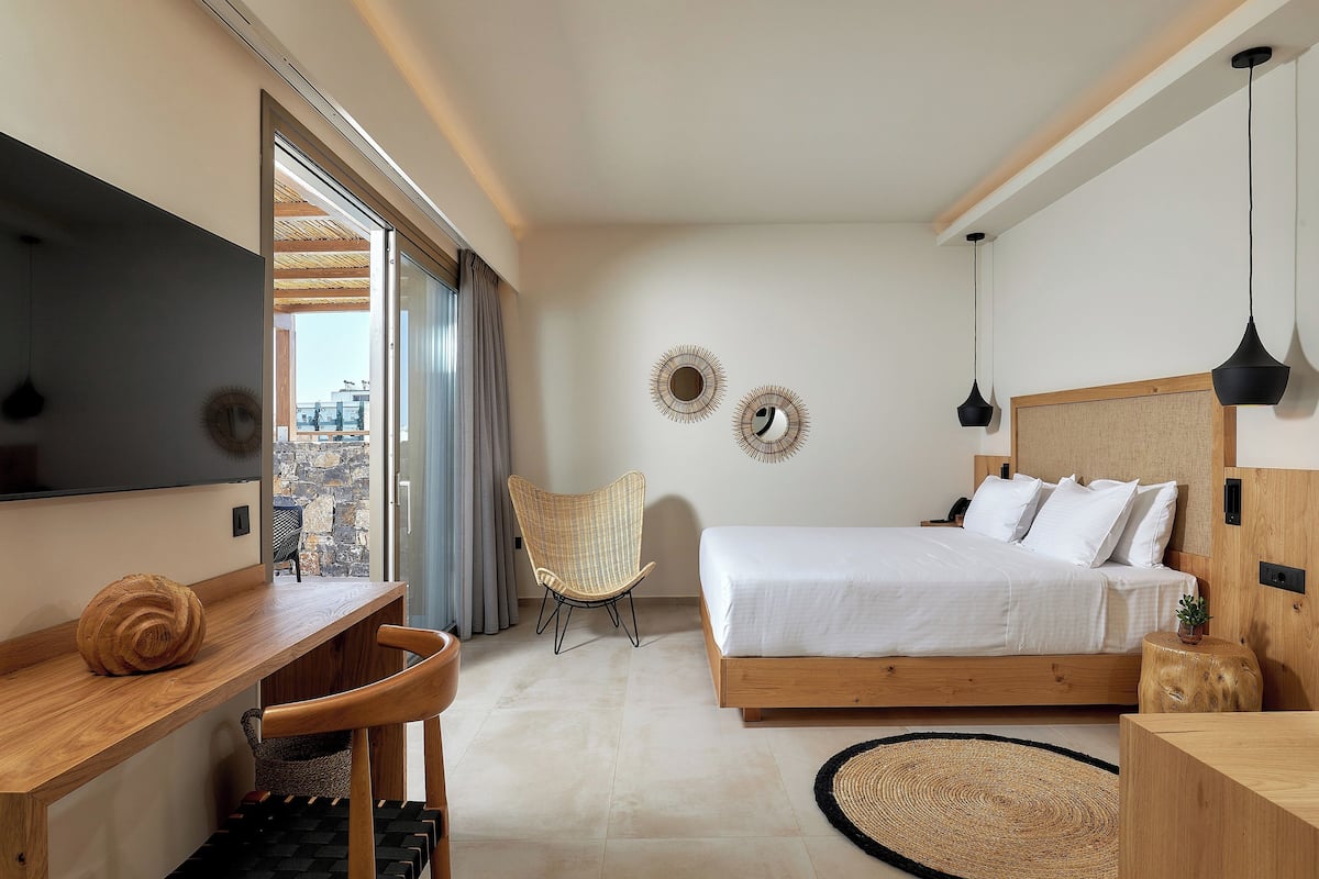 A modern bedroom with a bed, wooden desk, chair, and a TV.