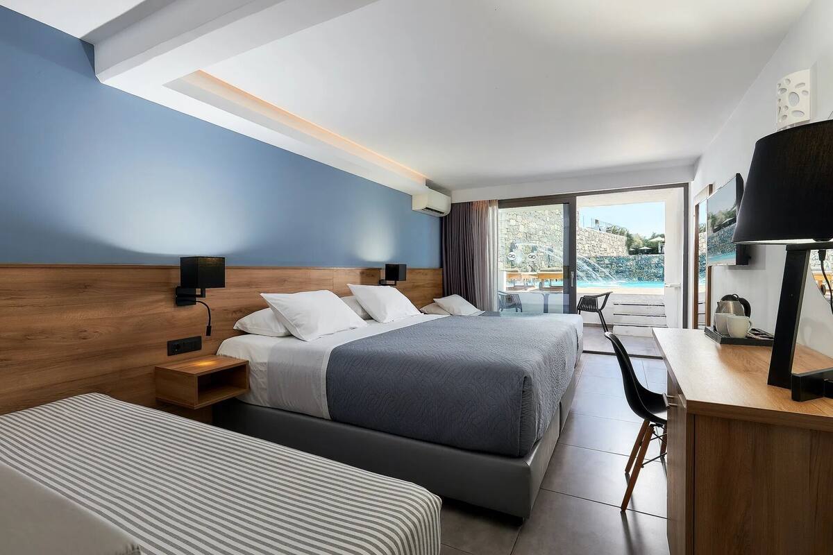 A modern hotel room with a large bed, a smaller bed, a desk, and a view of a pool.