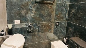 Een moderne badkamer met een marmeren spatwand, een toilet, een hygiëneschuimer en een wastafel.
