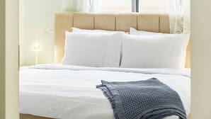 A neatly made bed with white bedding and a gray blanket, a beige headboard, and a bedside lamp. - MAMAD - Tranquil Galilee Retreat by Sea N' Rent (Merom HaGalil)
