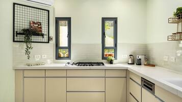 A modern kitchen with a gas stove, white countertops, beige cabinets, and two windows with black frames.