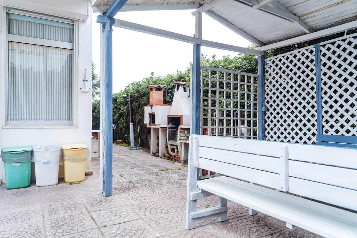 A covered outdoor area with a bench, a white building with a window, and a white fence with a lattice design.
