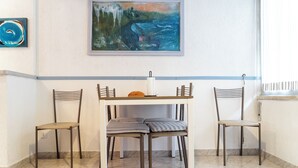 En matplats med ett bord och fyra stolar, en tavla på väggen och ett fönster med gardiner.