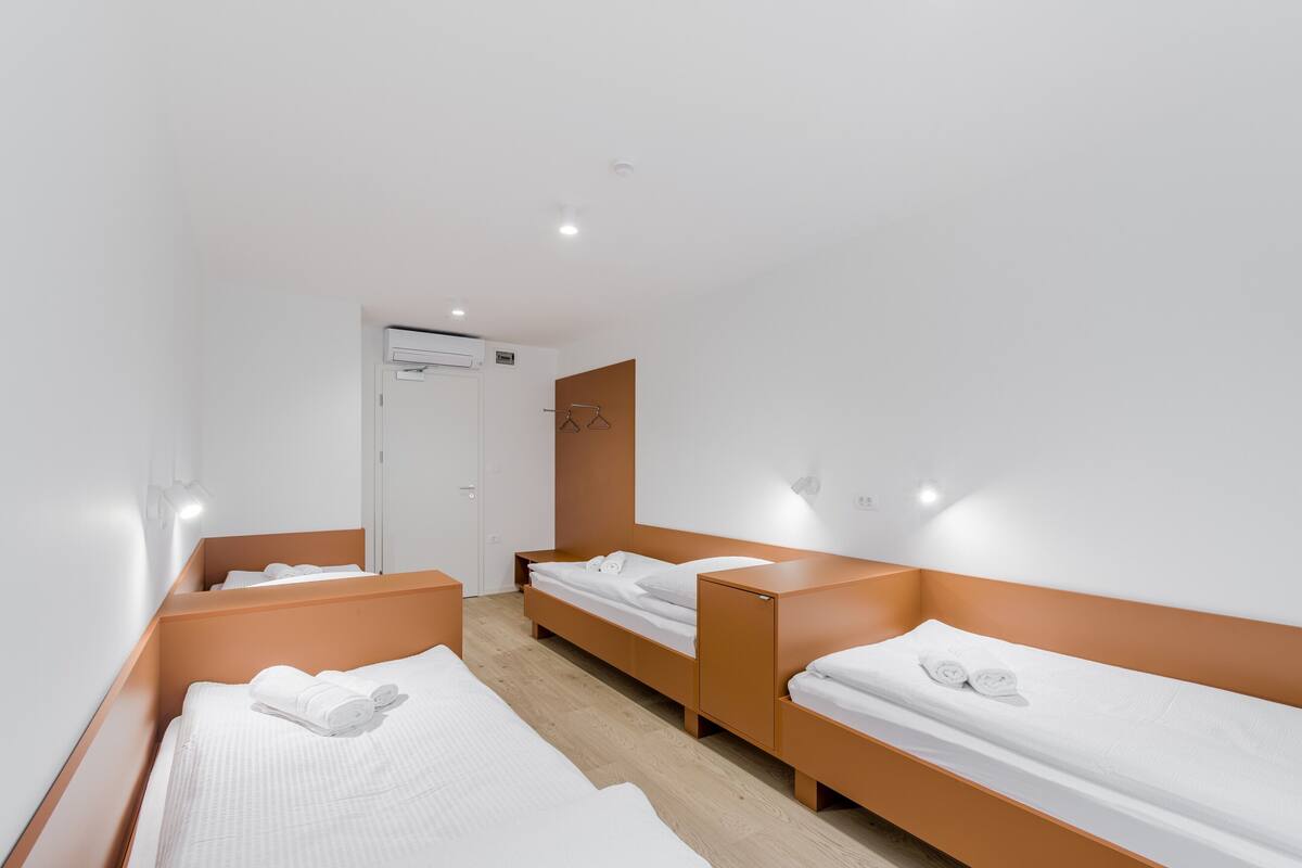 Une chambre d’hôtel avec trois lits simples, une armoire et un miroir.