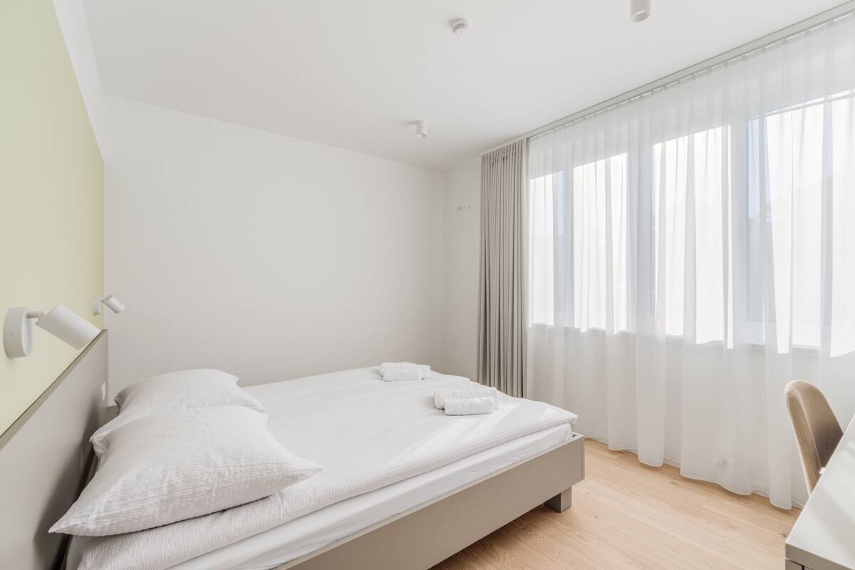 Une chambre d’hôtel au décor minimaliste, comprenant un lit simple, une table de chevet et une chaise.