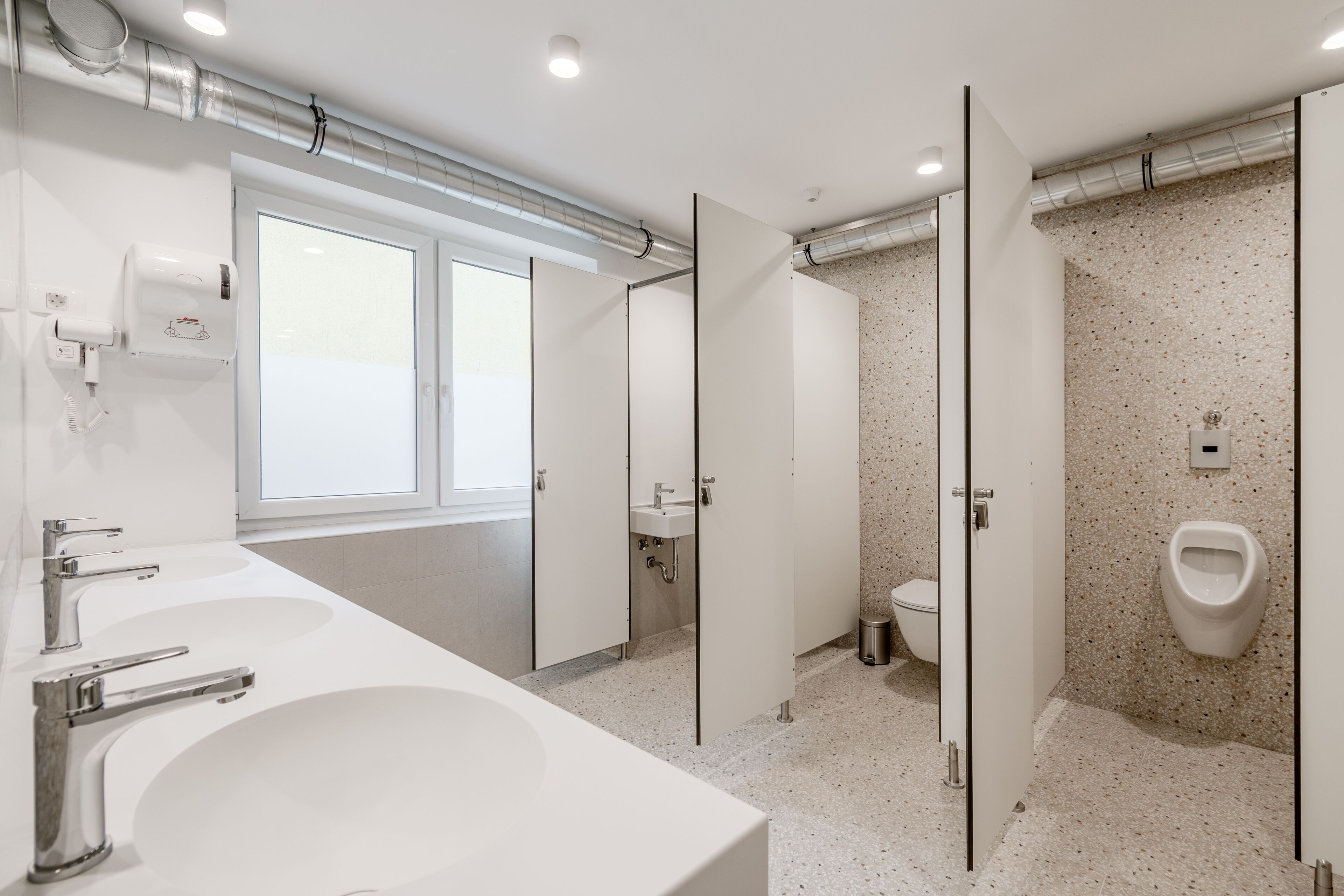 Uma casa de banho moderna com duas lavatórios, uma sanita e um urinol.
