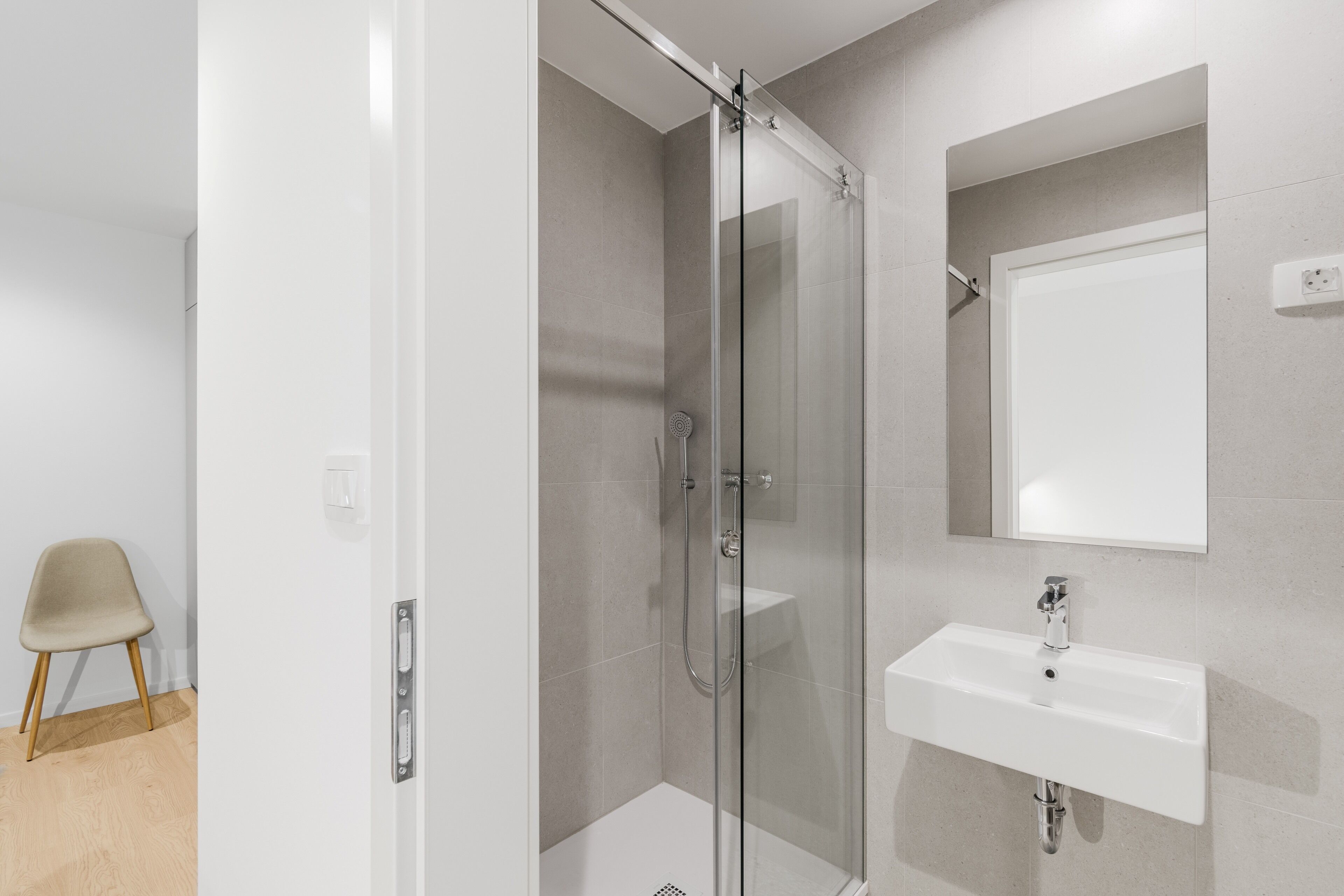 Une salle de bain moderne avec une douche à parois de verre, un lavabo blanc et un miroir au-dessus.