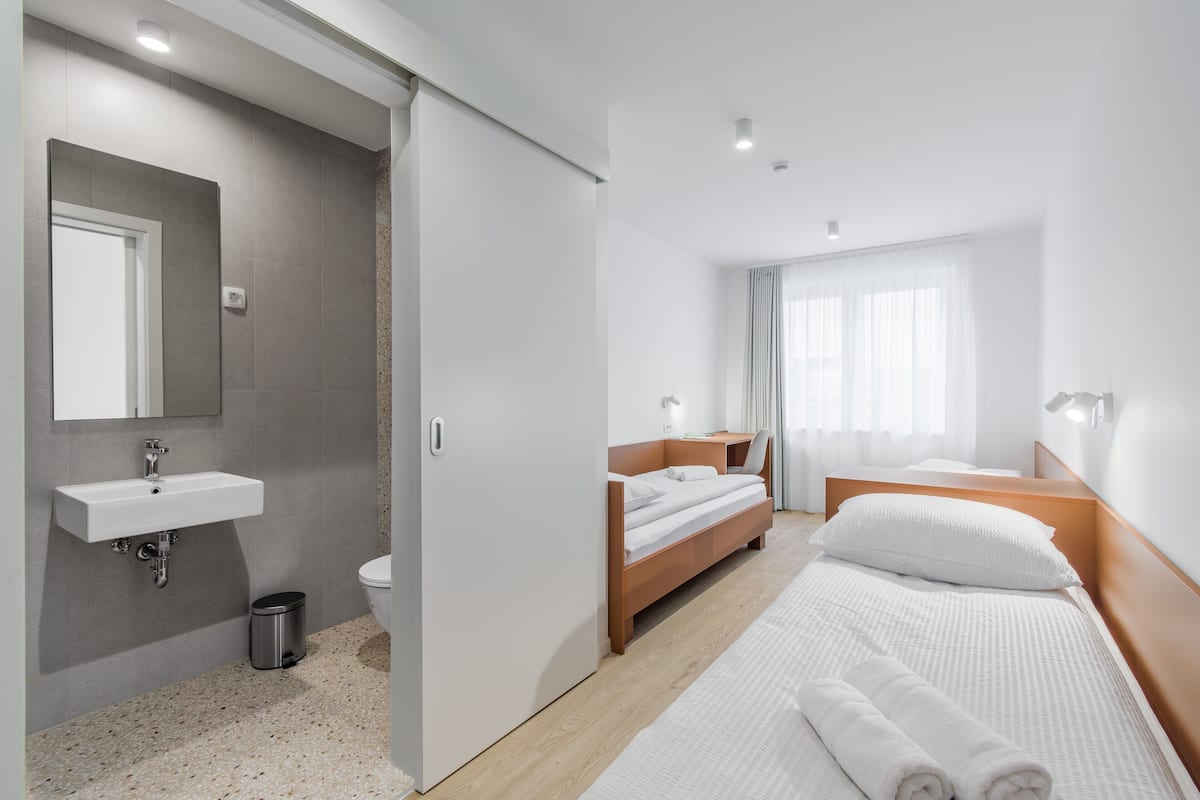 Une chambre d’hôtel moderne, dotée d’une salle de bain, d’un lit avec du linge de lit blanc et d’une table de chevet.