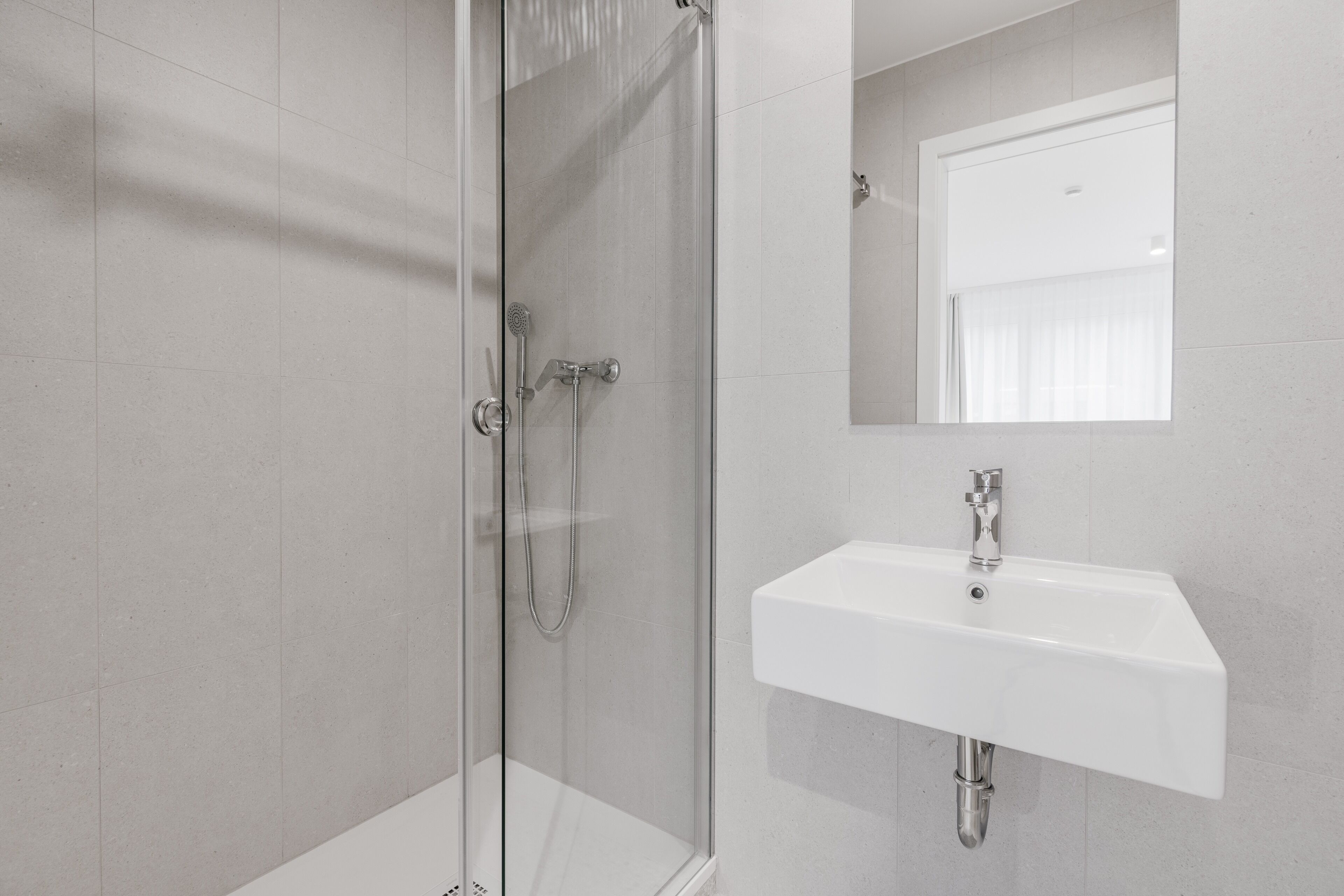 Une salle de bain moderne avec une douche à parois de verre, un lavabo blanc et un miroir au-dessus du lavabo.