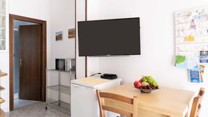 Una cocina con microondas, un refrigerador, una mesa de madera con sillas y un televisor de pantalla plana montado en la pared.