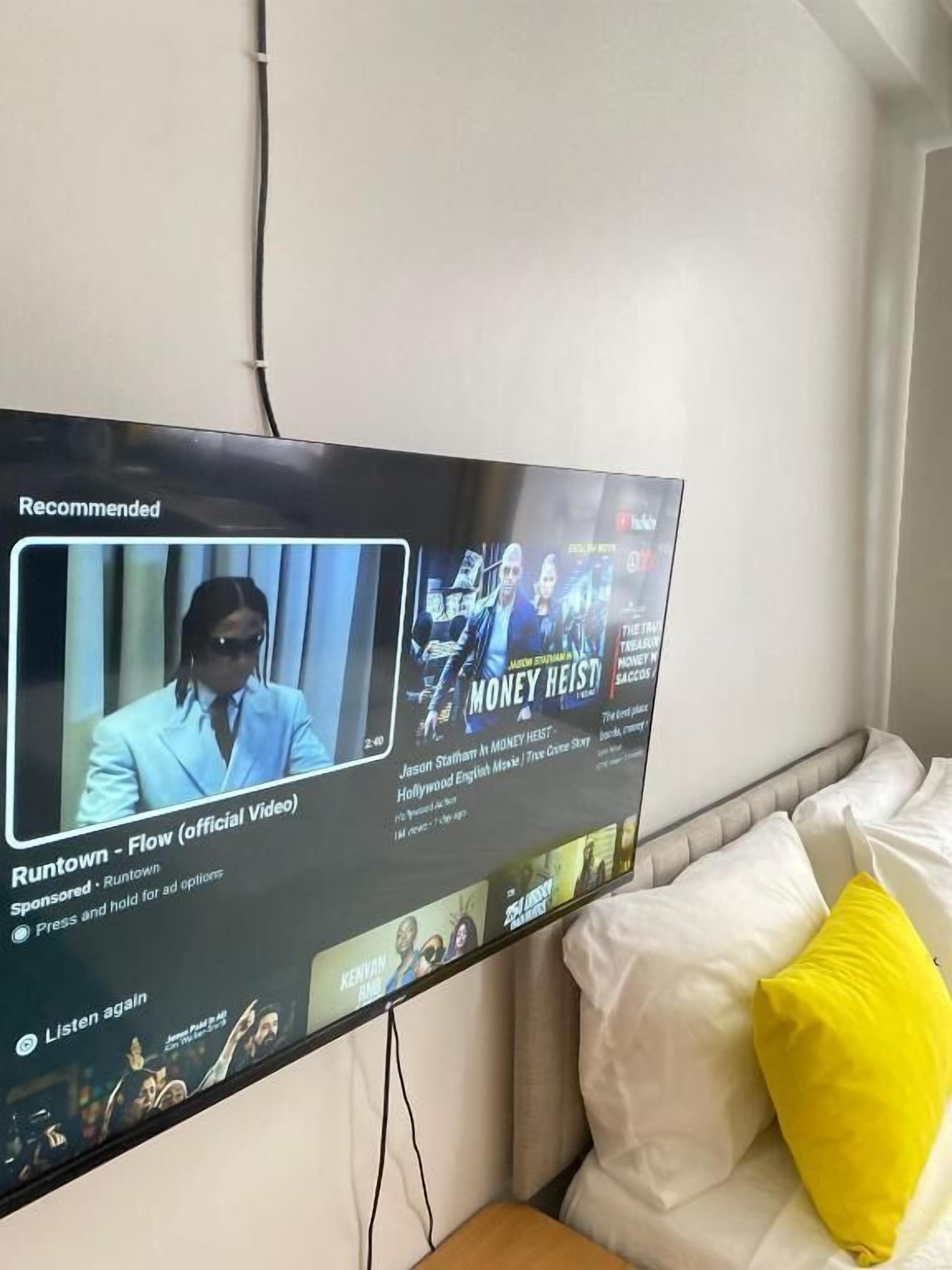 A television displaying a movie recommendation for 'Money Heist' and 'Runtown - Flow (official video)'.