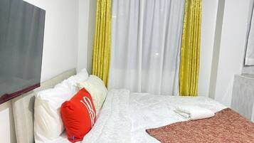 Ein Hotelzimmer mit einem Bett, weißer Bettwäsche, einem roten Kopfkissen und gelben Vorhängen.