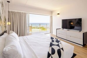 Une chambre d’hôtel dotée d’un grand lit, d’une télévision et d’un balcon offrant une vue sur la mer, le tout dans un décor moderne.