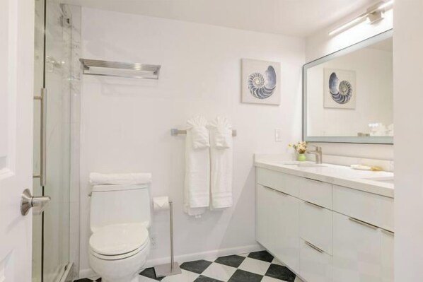A bathroom with a white toilet, a sink with a mirror, and two wall-mounted towel racks. - Newly Reno’d Oceanview Luxe Stay w/ Free Parking (Honolulu)