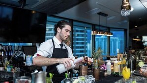 Ein Barkeeper bereitet Getränke an einer Bar mit Blick auf die Stadt zu.
