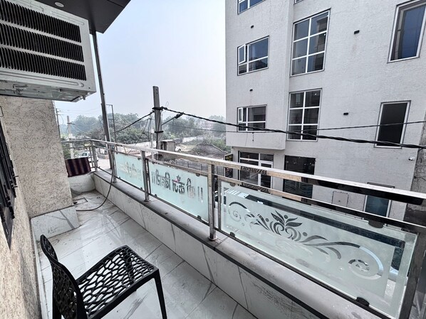 Un balcon avec une rambarde en métal, une porte vitrée et une chaise en métal.