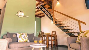 Un interior moderno con techo de madera, una escalera, un sofá, una mesa con vasos y un comedor.