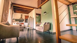Un espacio habitable amplio con techo alto, vigas de madera, una escalera y una cocina al fondo.