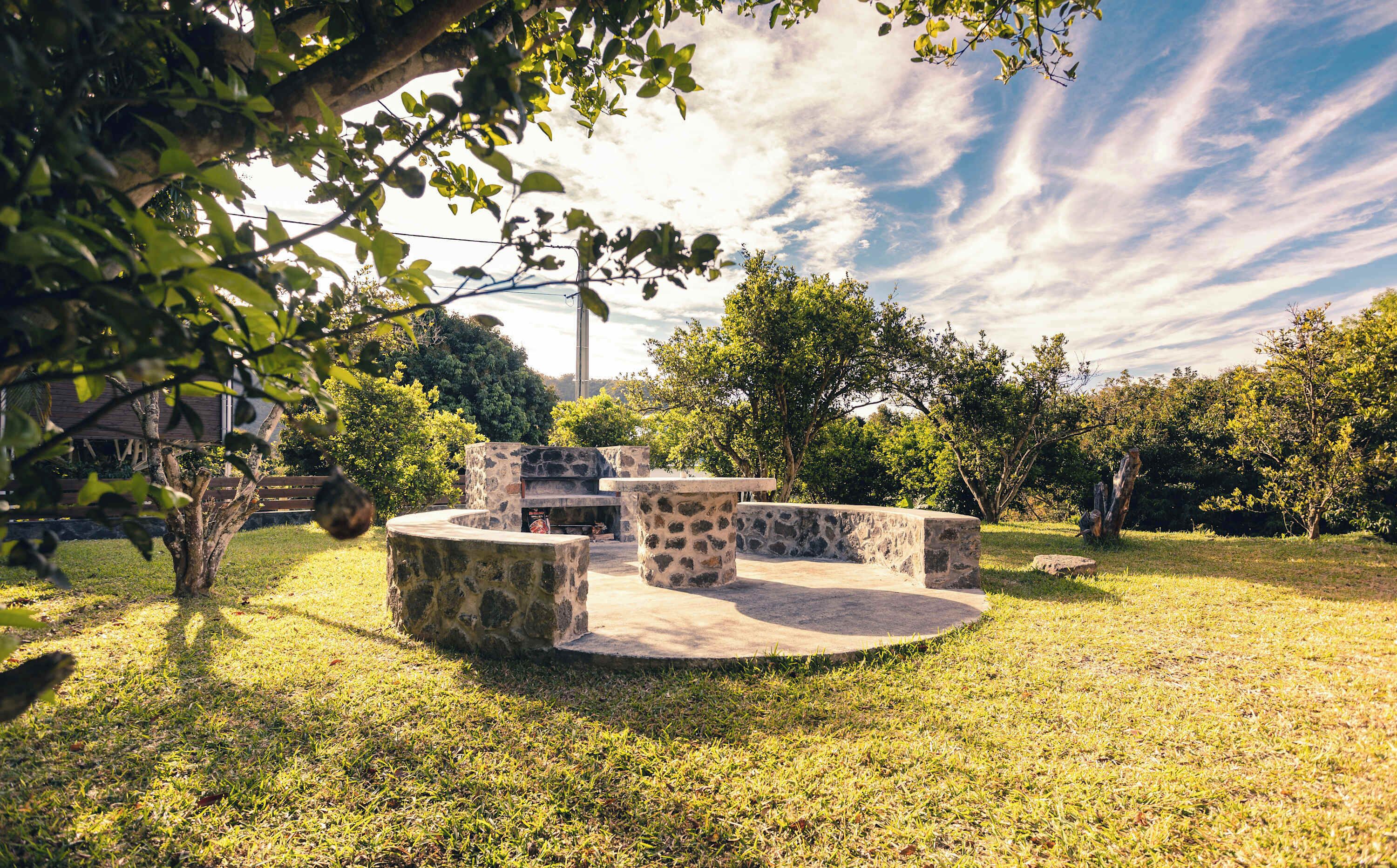 Un espace extérieur aménagé avec des tables et des chaises en pierre, entouré de pelouse et d’arbres.