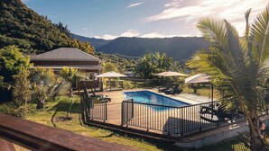 Una piscina con muelle de madera, rodeada de palmeras y montañas al fondo.