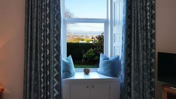 Une pièce dotée d’une baie vitrée, de meubles blancs et d’une petite table agrémentée de deux coussins bleus.