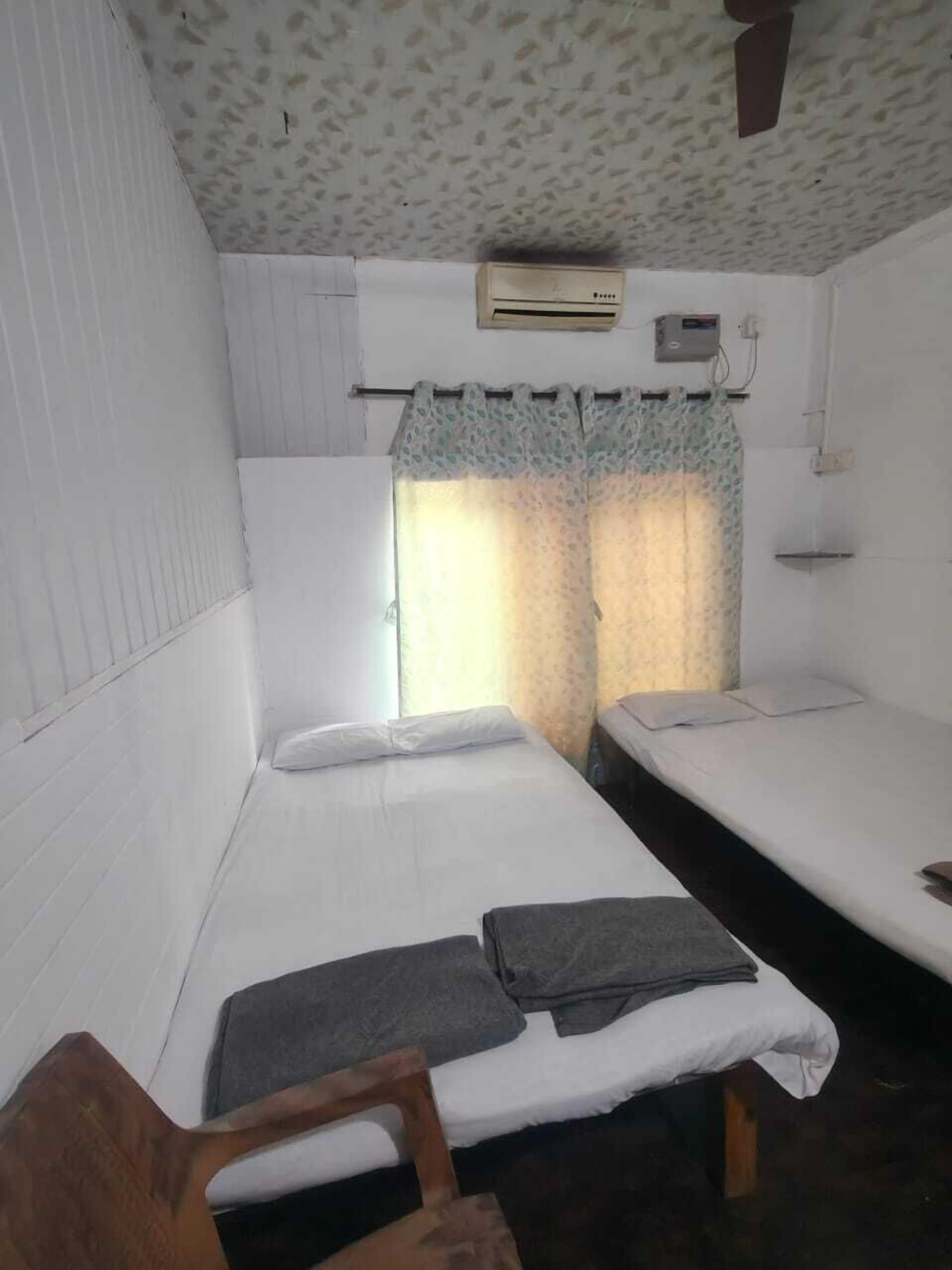 Een compacte, eenvoudige kamer met twee bedden, een stoel en een plafondventilator.