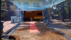 Un terrain de cricket délimité par un filet bleu, avec un tapis rouge au centre.