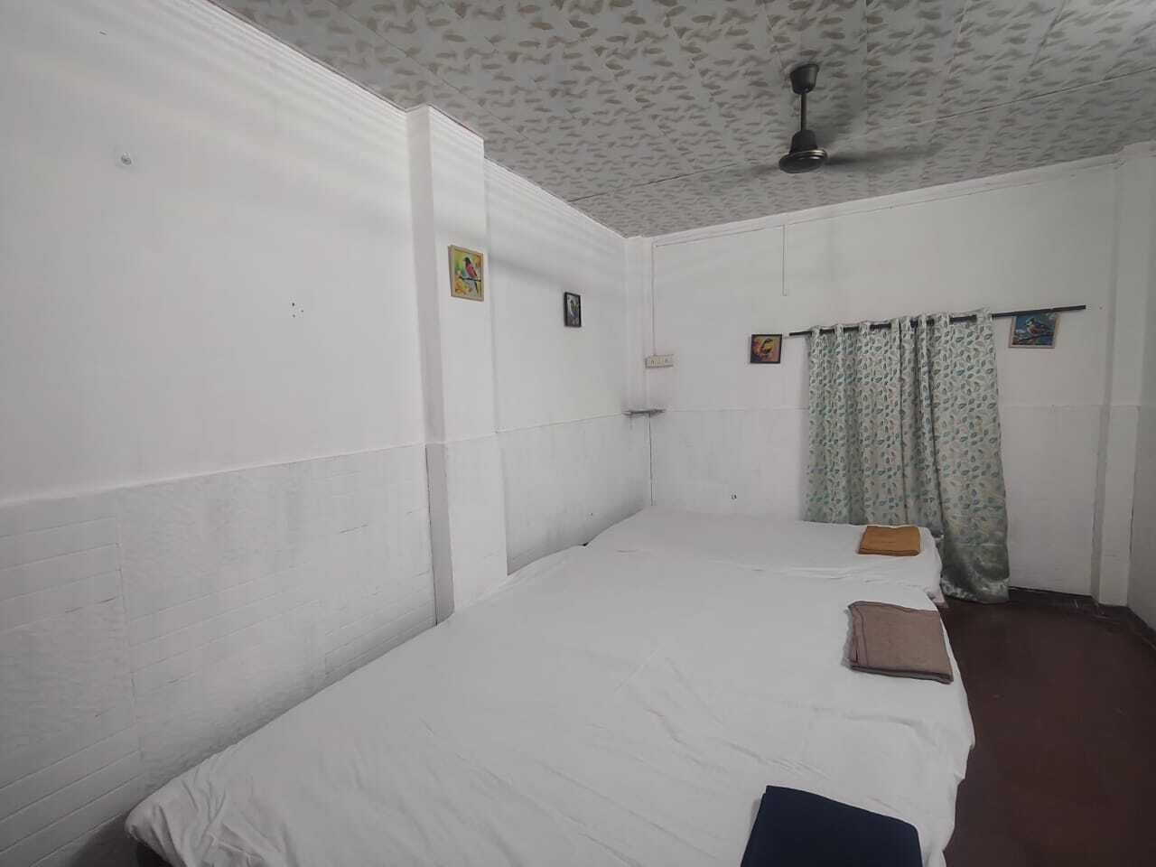 Una habitación con una cama individual, ventilador de techo y ventana con cortinas estampadas.