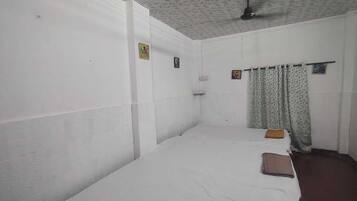 Una habitación con una cama individual, ventilador de techo y ventana con cortinas estampadas.